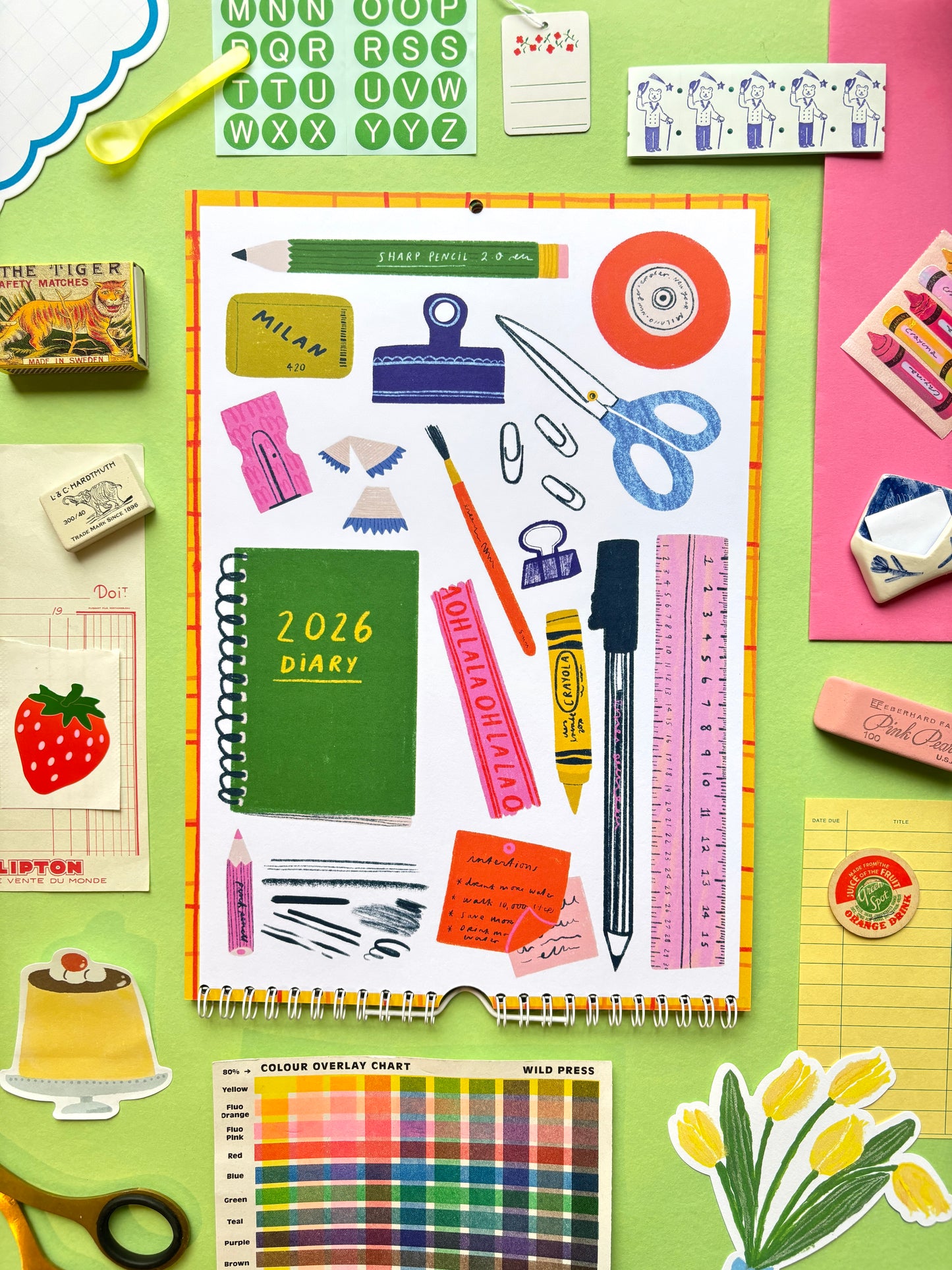 Collection of stationery items including a diary, scissors, crayons, and clips on a colorful background.