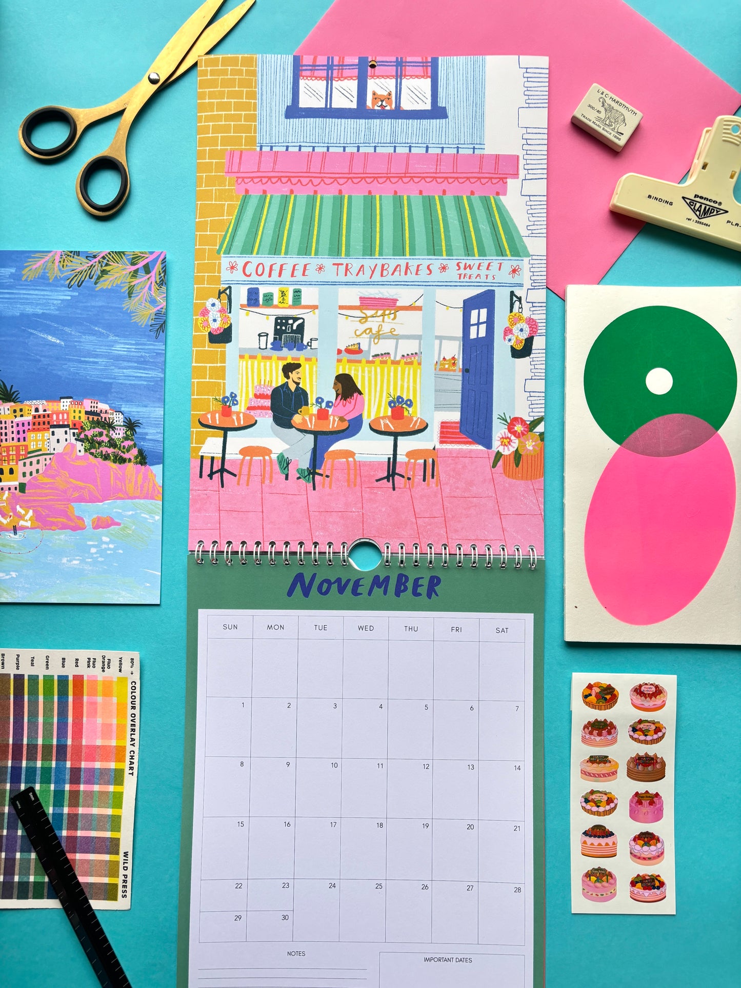 Calendar with a colorful illustration of a street scene, surrounded by stationery items on a blue background.
