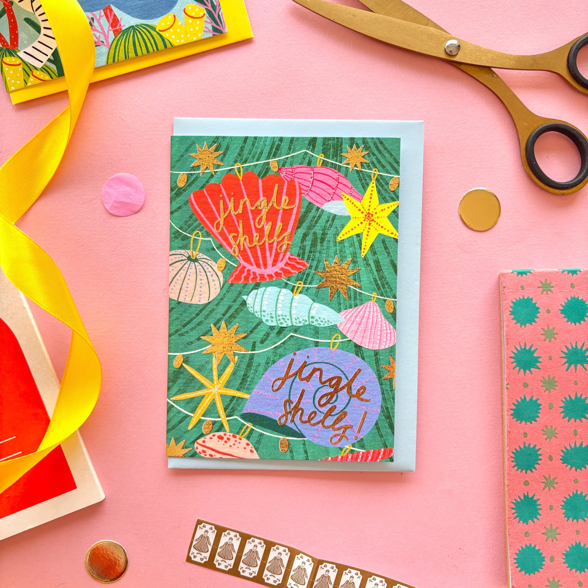 A christmas card with colourful shell lights around a colourful christmas tree surrounded by gold stars and hand-written text jingle bells, jingle bells – festive ocean-themed holiday card with bright yellow border on pastel background.