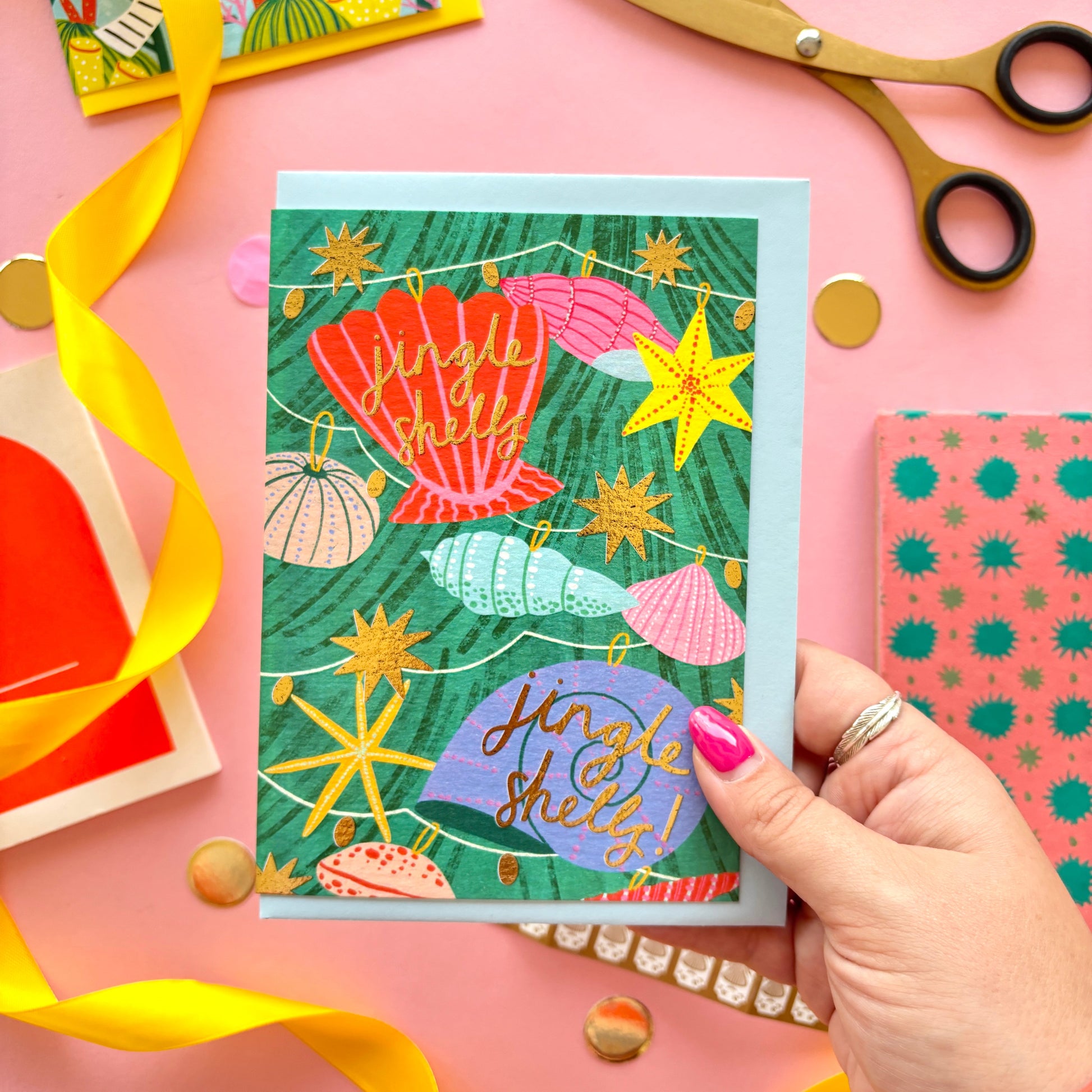 A christmas card with colourful shell lights around a colourful christmas tree surrounded by gold stars and hand-written text jingle bells, jingle bells – festive ocean-themed holiday card with bright yellow border on pastel background.