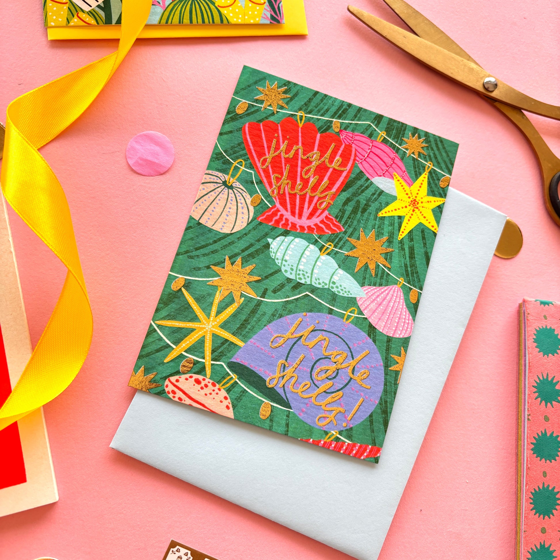 A christmas card with colourful shell lights around a colourful christmas tree surrounded by gold stars and hand-written text jingle bells, jingle bells – festive ocean-themed holiday card with bright yellow border on pastel background.