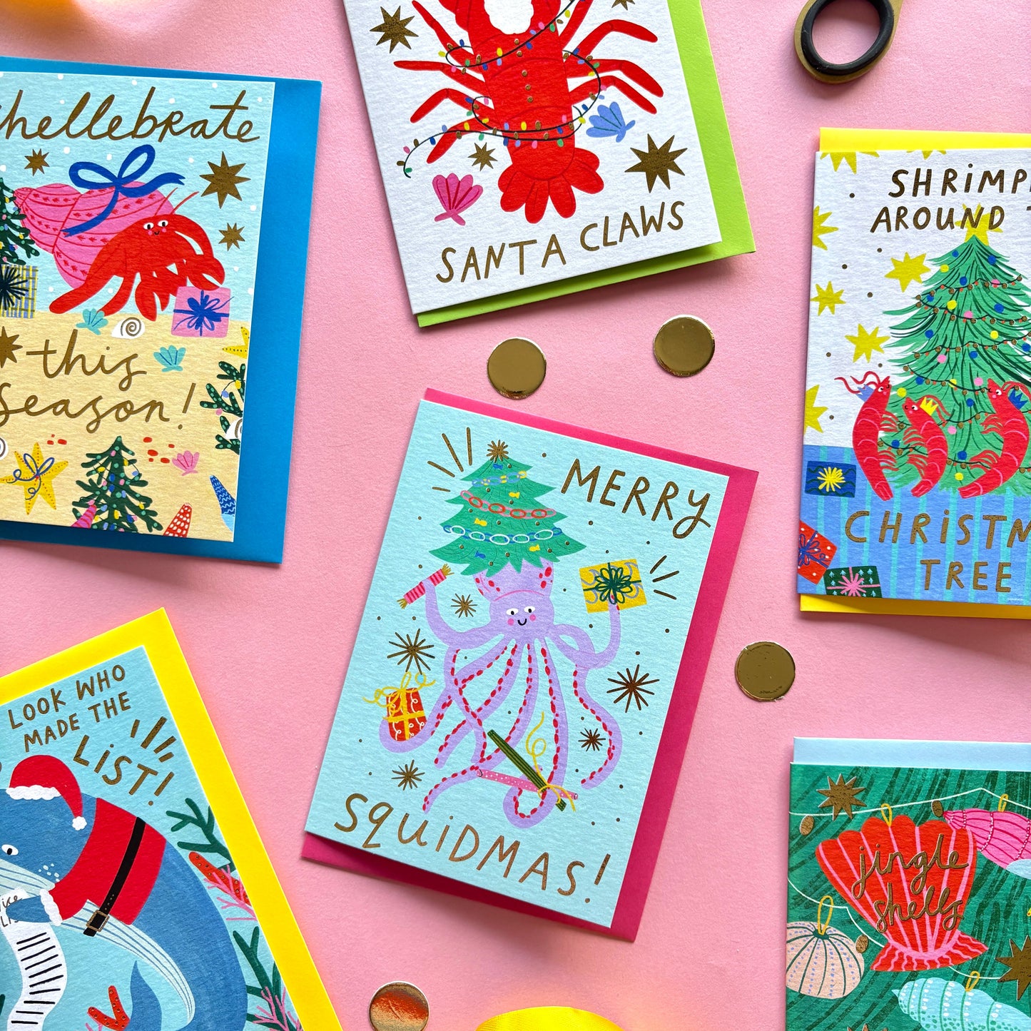 Colorful Christmas-themed greeting cards on a pink background with scissors and ribbons.