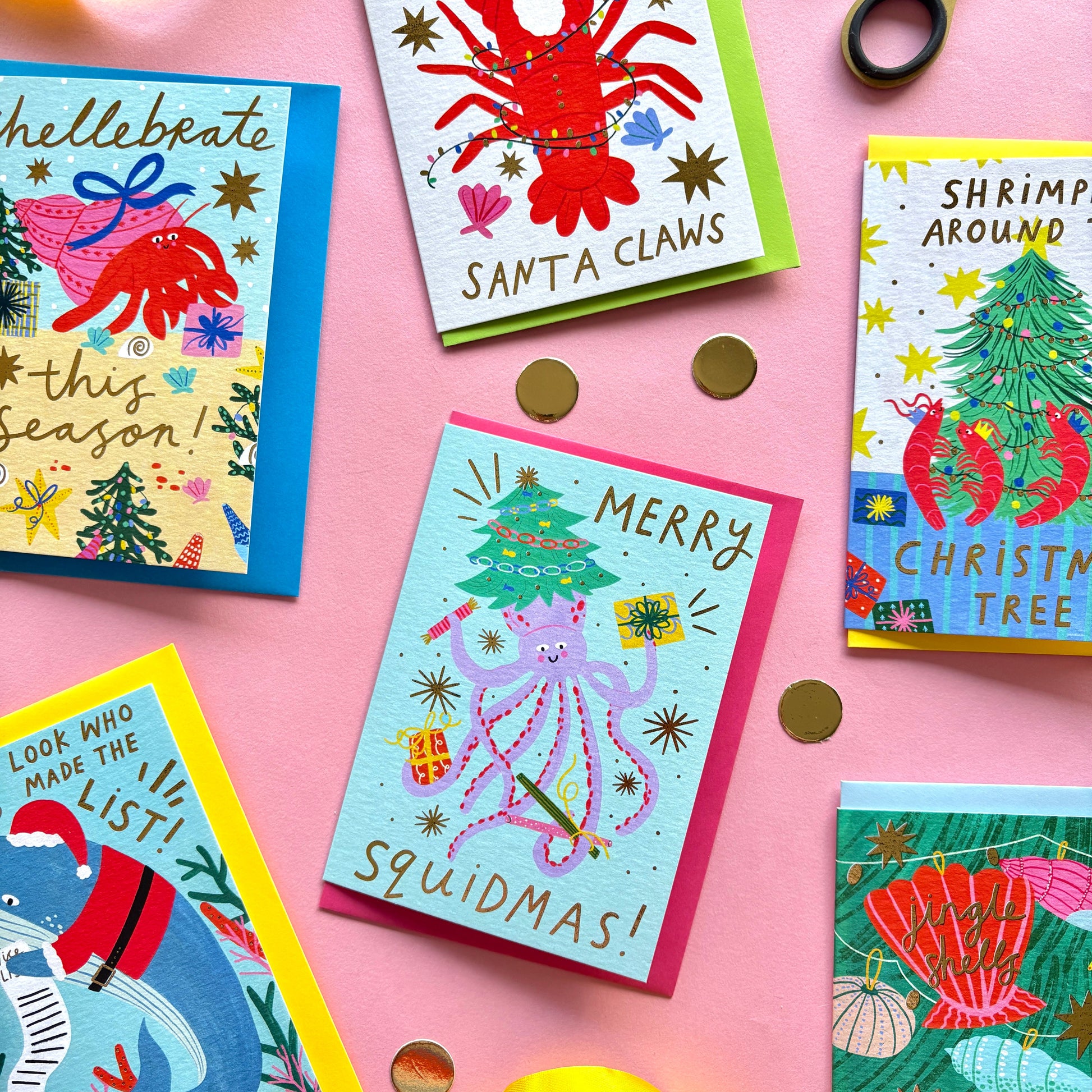 Colorful Christmas-themed greeting cards on a pink background with scissors and ribbons.