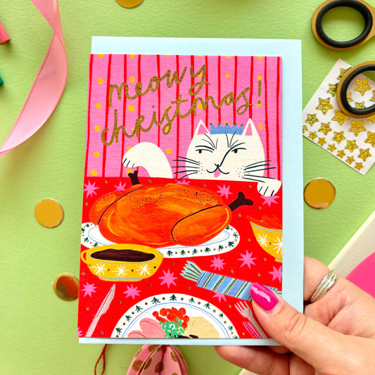 ‘Meowy Christmas’ funny cat Christmas card showing a naughty cat licking its lips at a festive dinner table with turkey and gold foil details