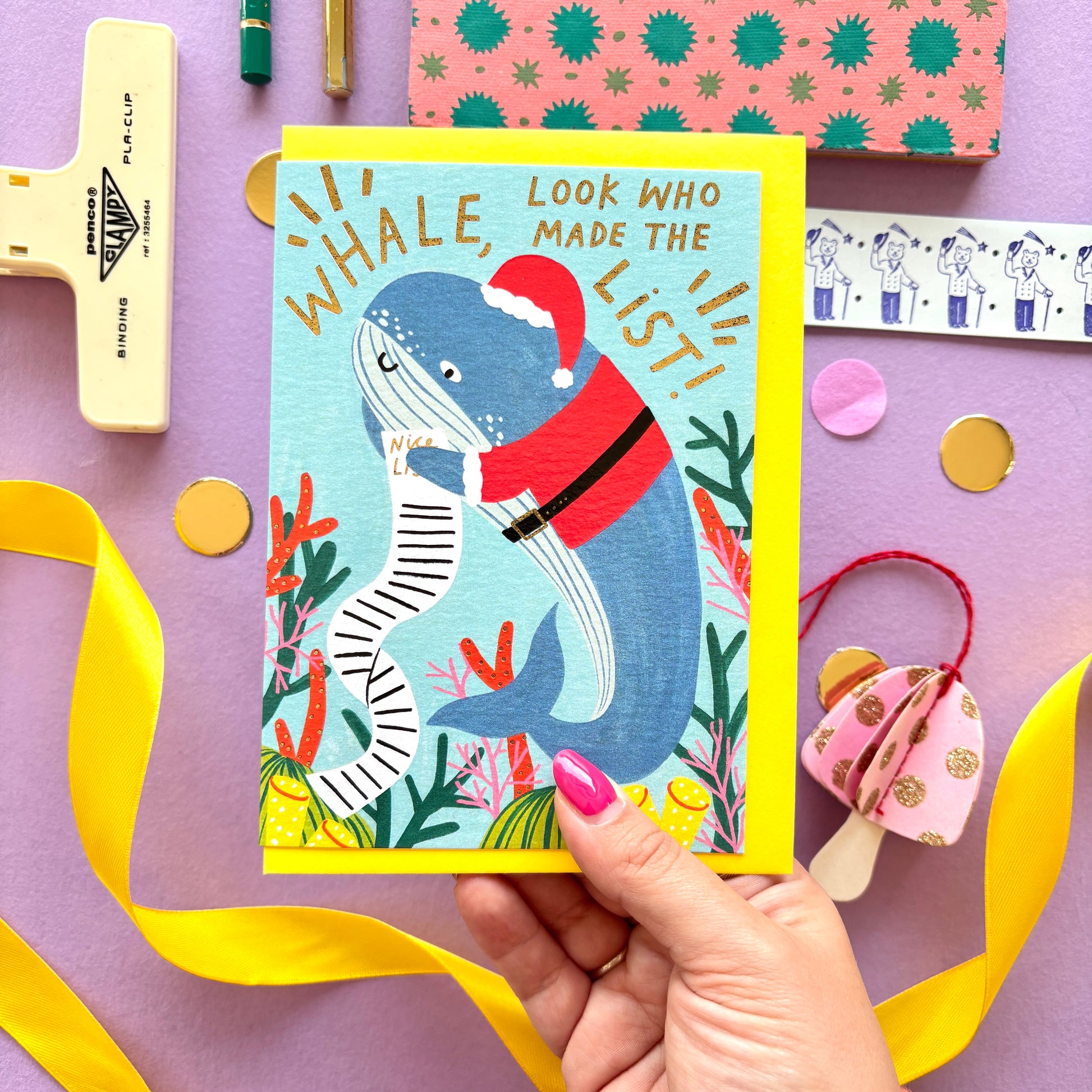 Funny Christmas card with a whale dressed as santa claus holding a long naughty and nice list surrounded by colourful coral along the reef- festive ocean-themed holiday card with bright blue background