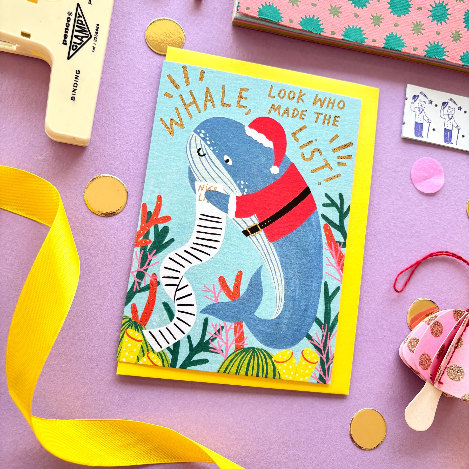 Funny Christmas card with a whale dressed as santa claus holding a long naughty and nice list surrounded by colourful coral along the reef- festive ocean-themed holiday card with bright blue background