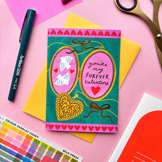 A picture of an illustrated valentines card by Kerrie McNeill a Northern irish illustrator. There is a locket with the words you're my favourite valentine on one side and the other are two doves surrounded my hearts.