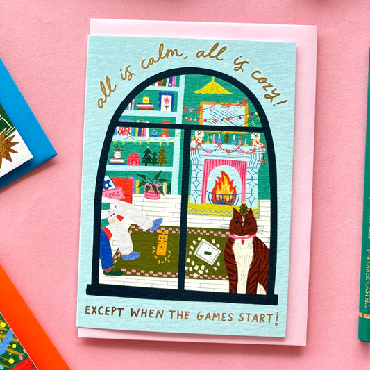 All Is Calm, All Is Cozy...Except When the Games Start Funny Christmas Card | Cozy Living Room Scene with Cat, Fireplace & Gold Foil | Family Game Night Christmas Card