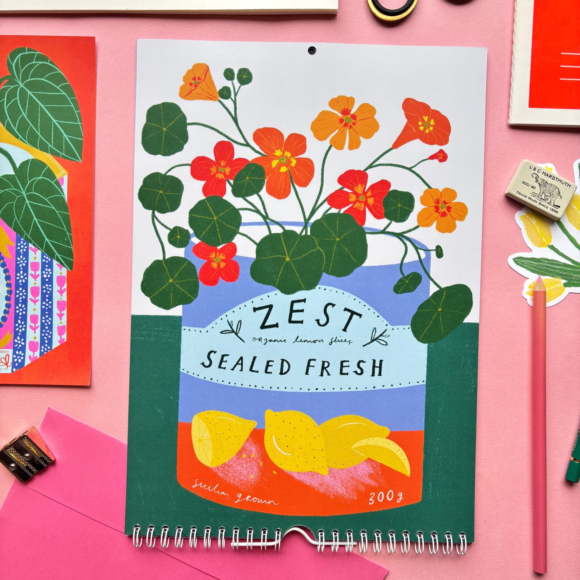 Floral-themed calendar titled 'Zest' on a pink background with stationery items.