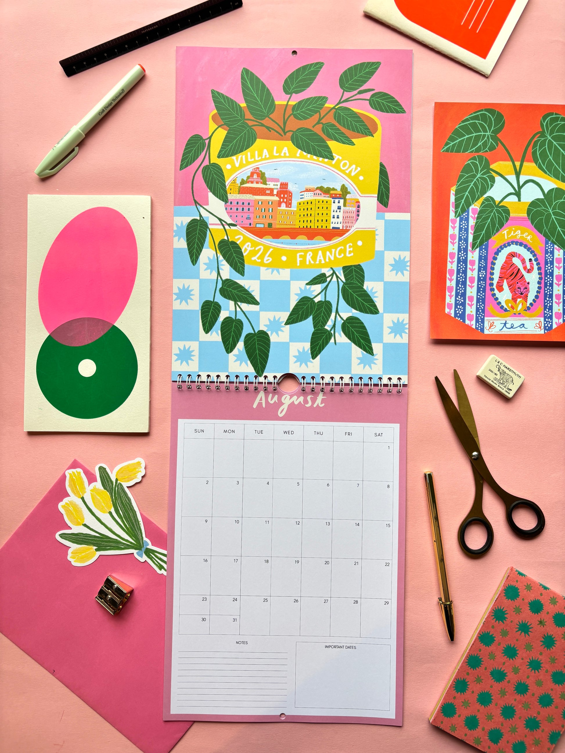 Colorful calendar with artistic design on a pink surface with stationery items.